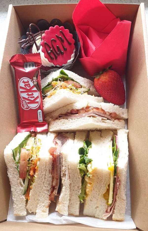 Box containing sandwiches, chocolate, fruit and a cake