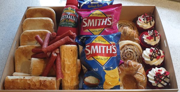 A box containing pies, sausage rolls, tomato sauce, savoury snacks, pastries and cakes